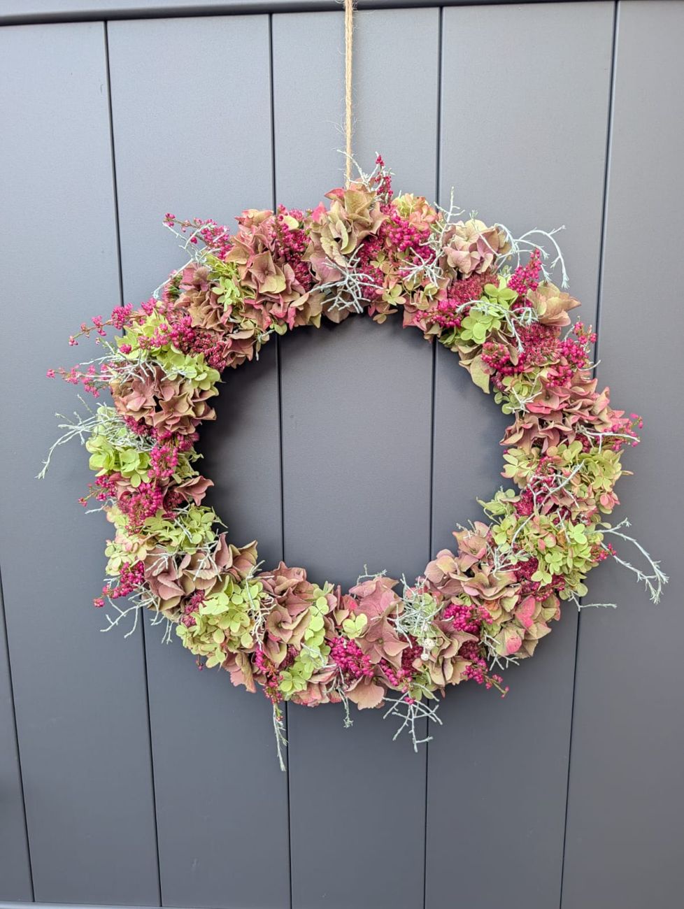 Handgebundener Herbstkranz aus Hortensien und Sedum an einer grauen Tür